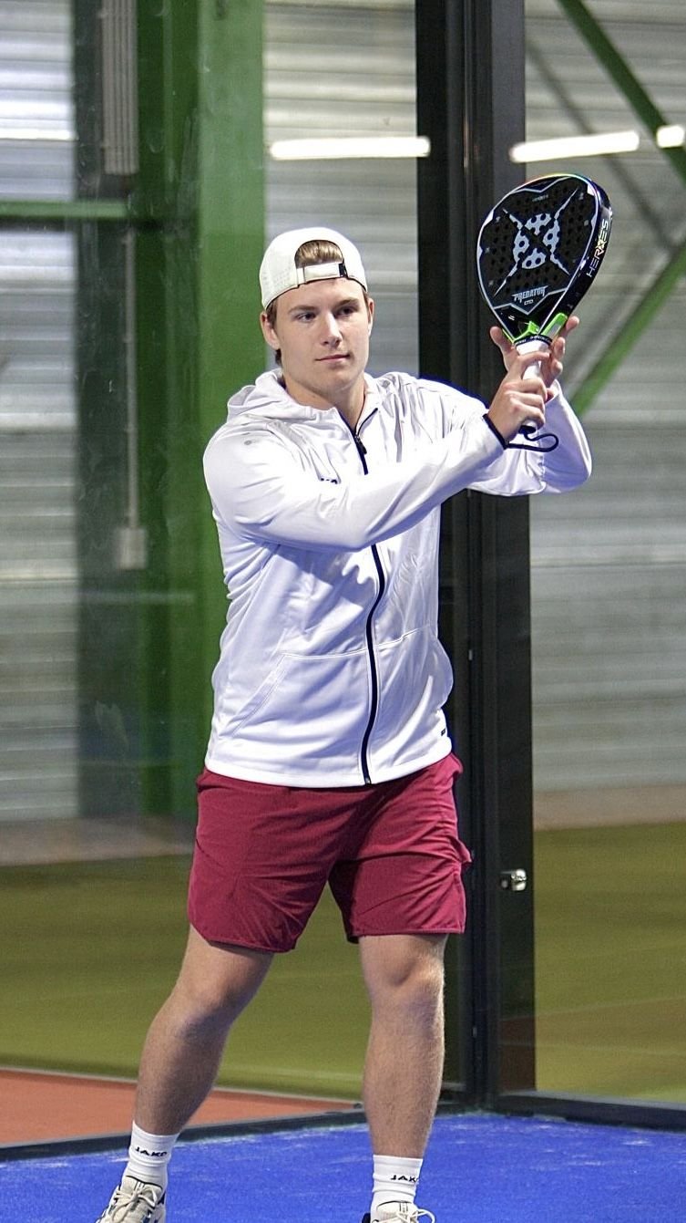 Matteo on court in a white JAKO jacket, holding the Heroes Predator LTD up in front of him